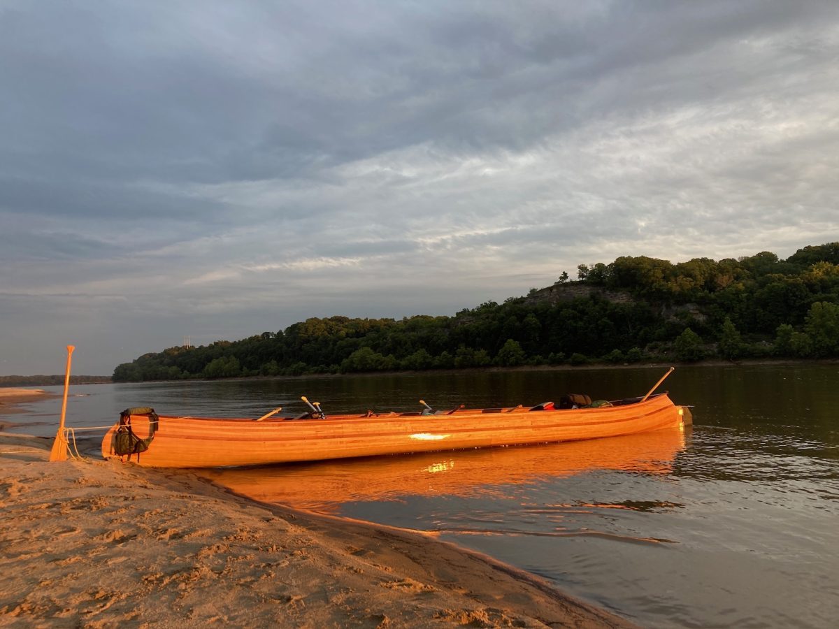 a wooden canoe sits on a sand bank along the Missouri River at sunset