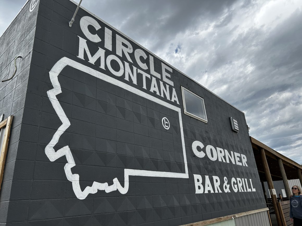 The side of a brick building painted black with a mural and the words Circle Montana on it and the outline of the state of Montana