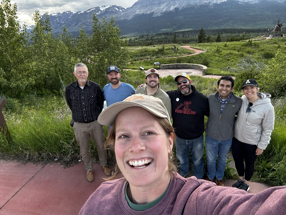 Emily Lytle takes a selfie standing above a group of people with mountains in the background