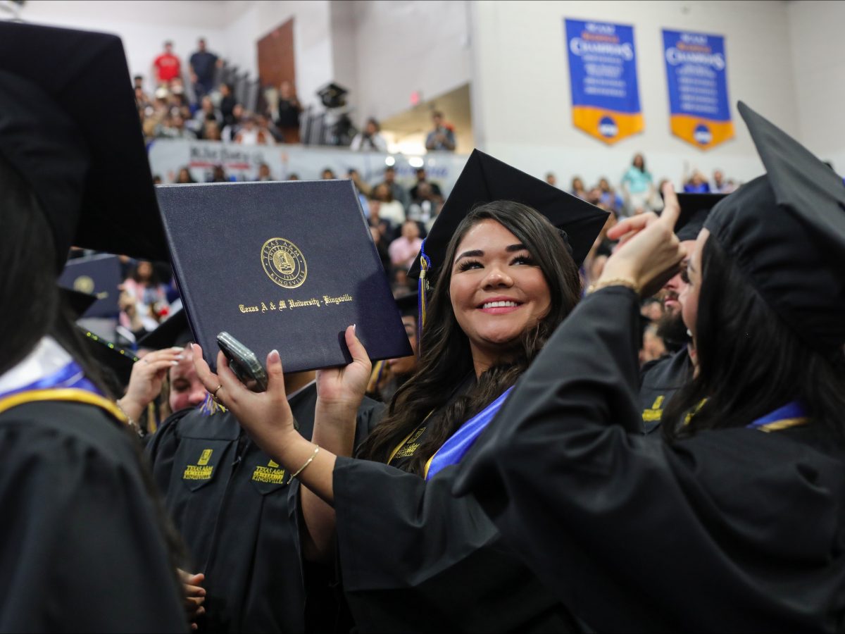 A college graduate at Texas A&M university holds up a diploma folder at a graduation ceremony in cap and gown